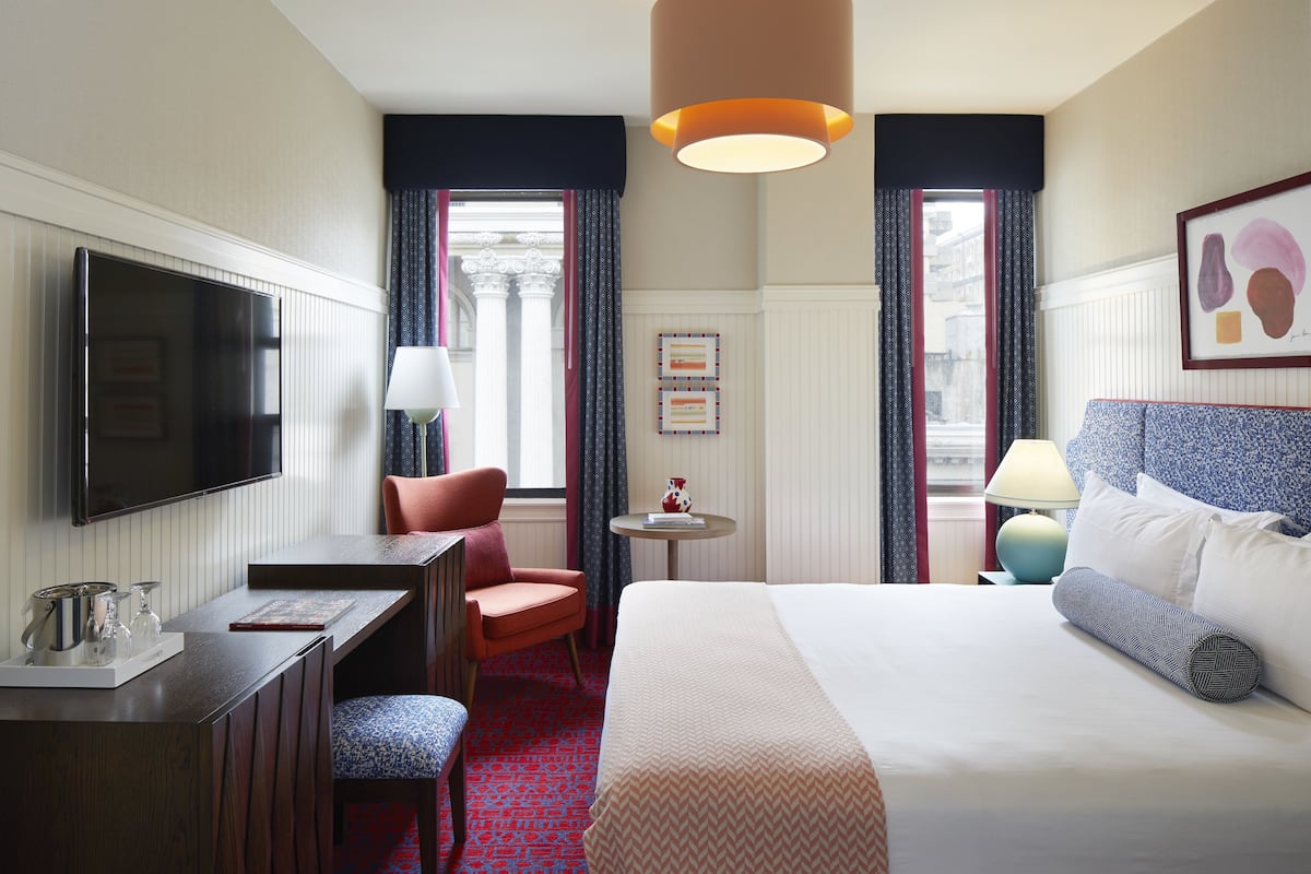A hotel room with a bed, a desk, a chair, a TV, and a window with curtains.