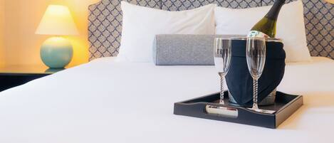 A hotel room with a bed, a tray with two champagne glasses and a bottle, a lamp, and framed artwork on the wall.