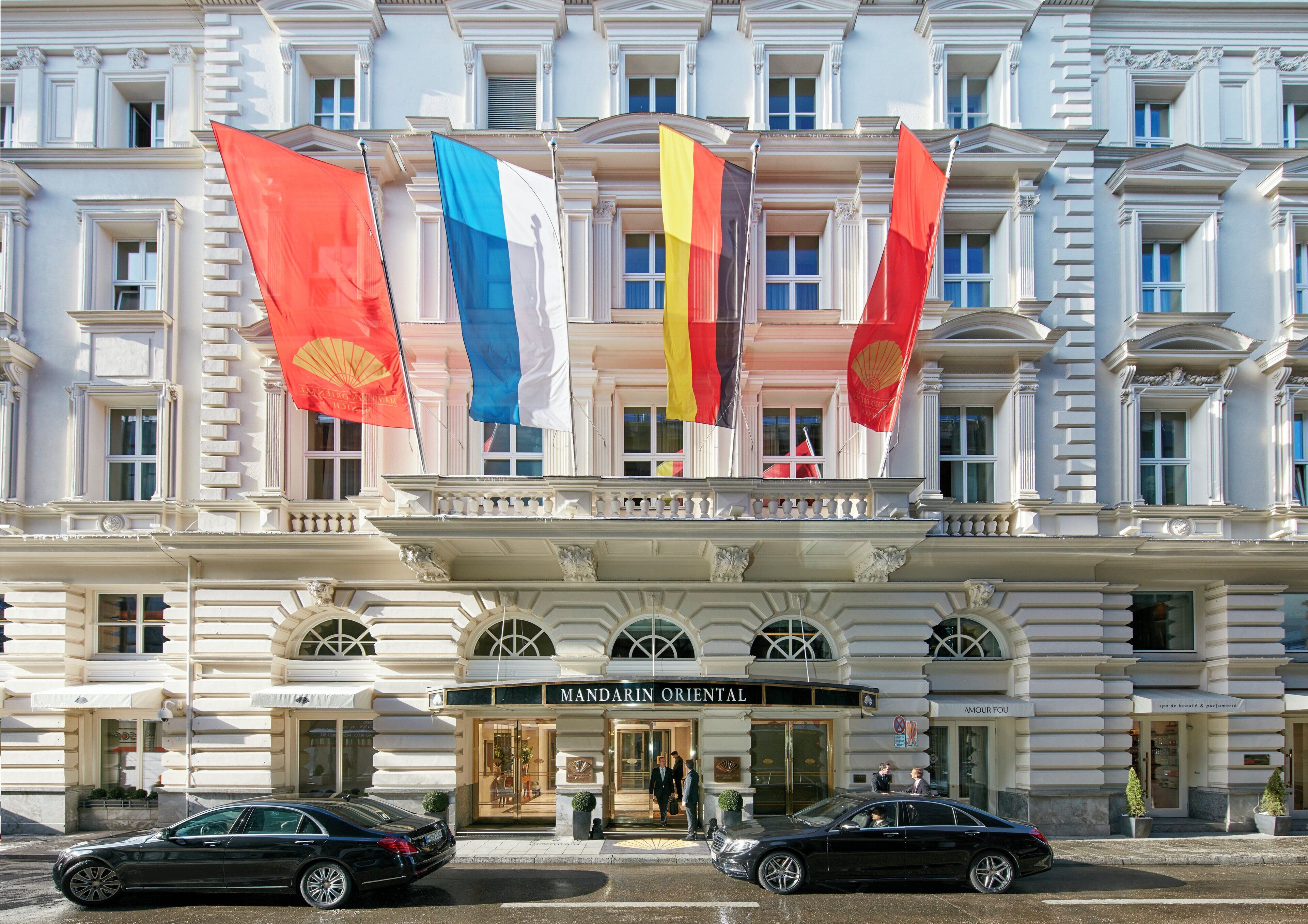 A hotel with multiple flags, a grand entrance, and two cars parked in front.