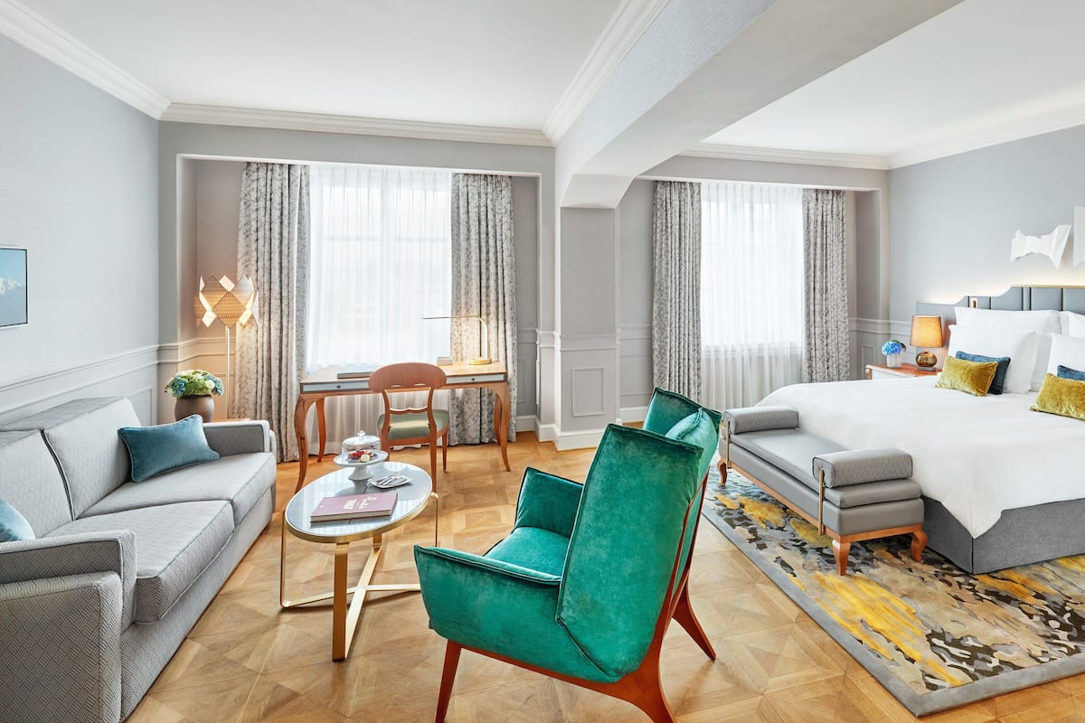 A modern hotel room with a bed, a sofa, a dining table, and a chair.