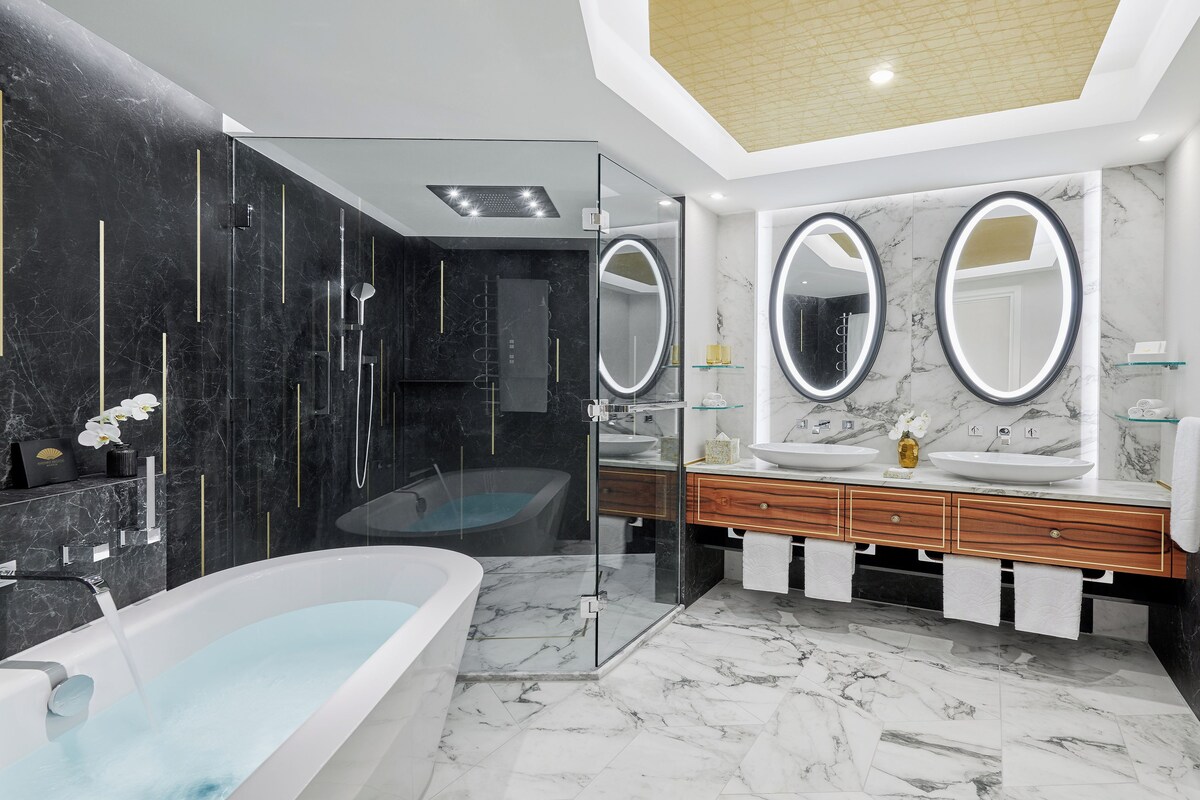 A modern bathroom with a freestanding bathtub, two sinks with round mirrors, and a glass-enclosed shower area.