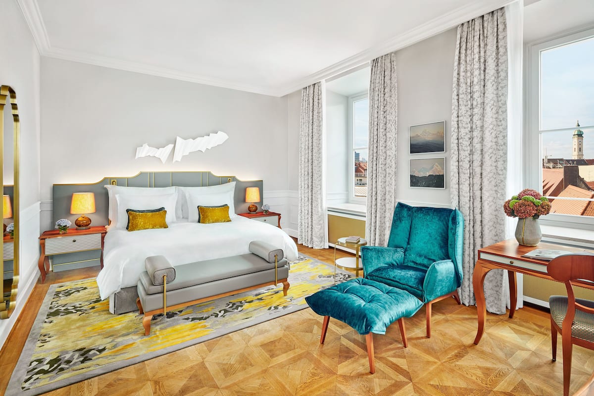 A hotel room with a large bed, a sitting area with a chair, a small table, and a view of the city.