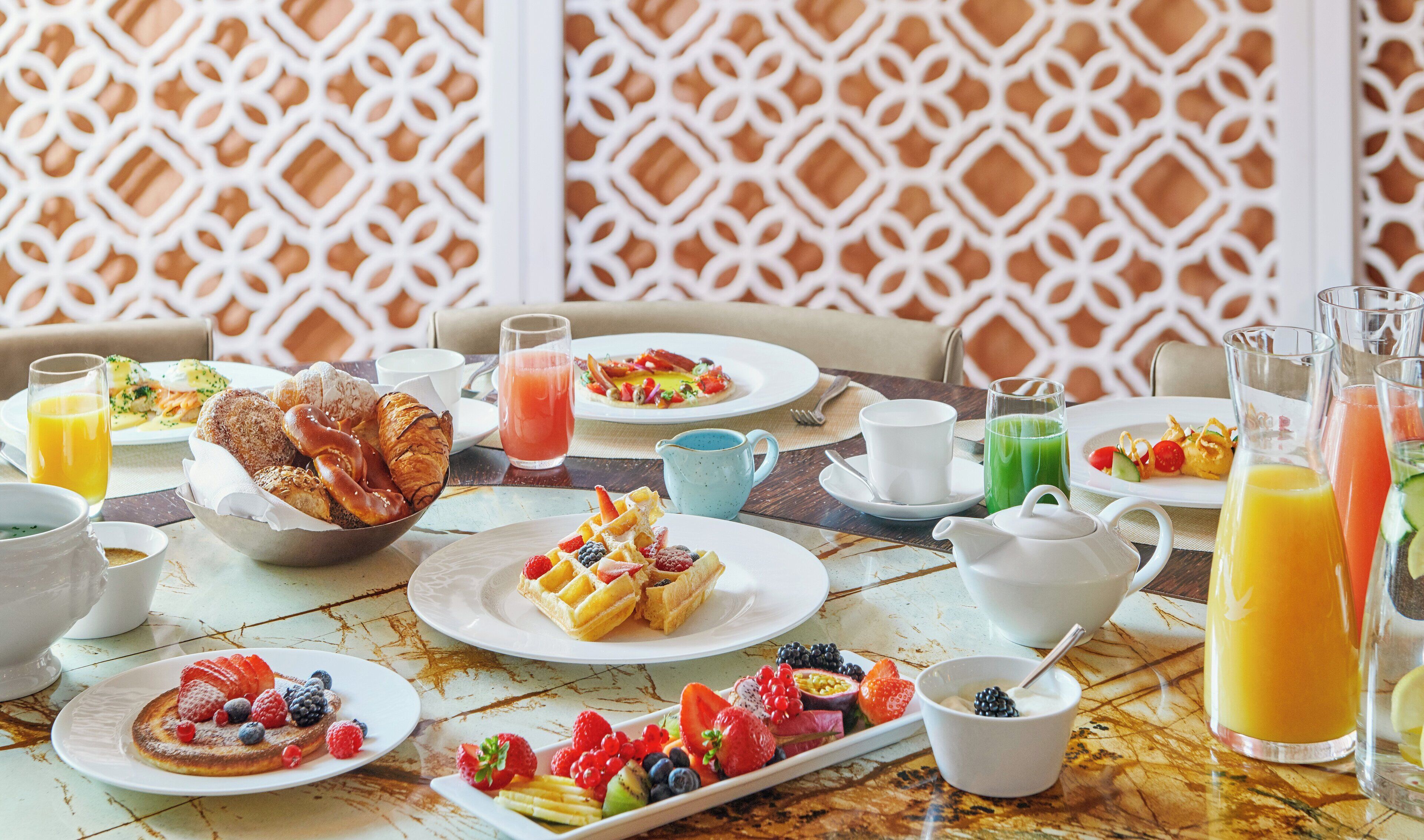 Una escena de desayuno con diversos platos, bebidas y una pared decorativa.