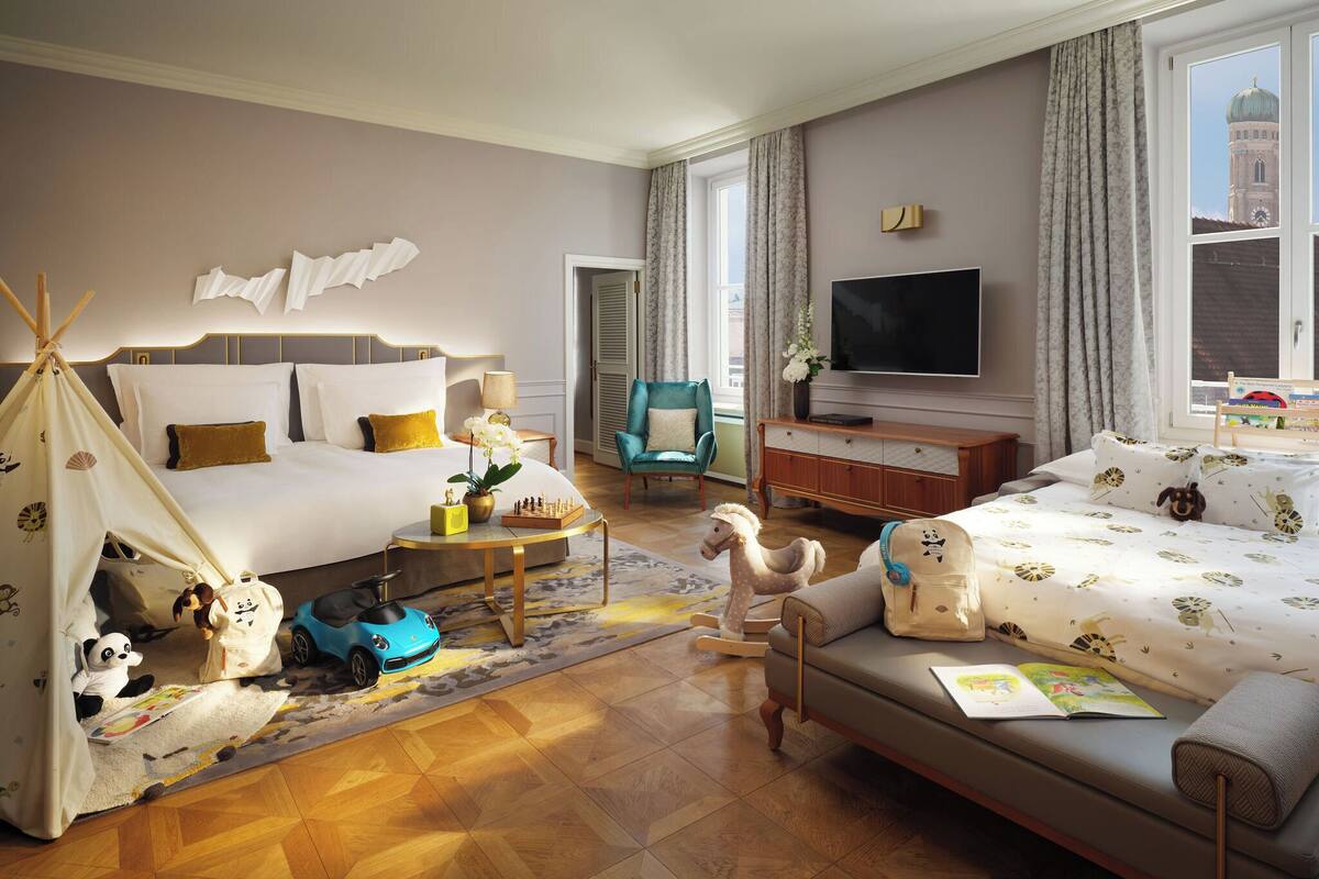A hotel room with a bed, sofa, TV, and a view of a building.