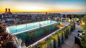 A rooftop pool with a view of a cityscape and a sunset.