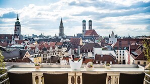 Una terraza con una mesa preparada para una comida, con vistas a un paisaje urbano con edificios históricos y un cielo despejado.