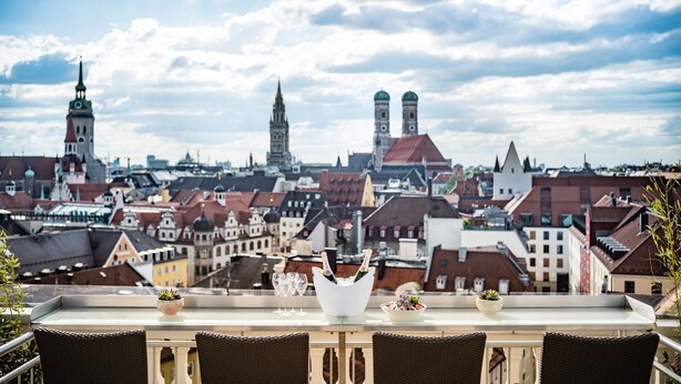 A terrace with a table set for a meal, overlooking a cityscape with historic buildings and a clear sky. - Mandarin Oriental, Munich (Munich)