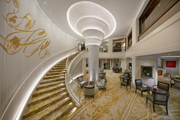 A spacious lobby with a grand staircase, comfortable seating areas, and a modern chandelier.