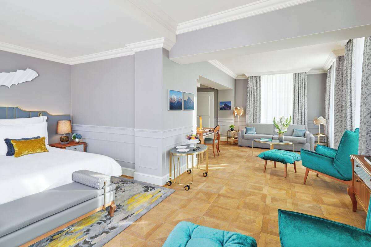 A hotel room with a bed, a sofa, a dining area, and a living room.