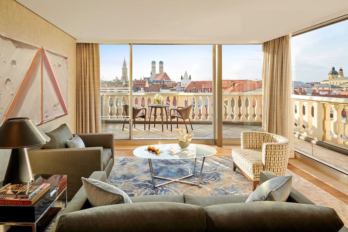A modern hotel room with a large balcony, furnished with a sofa, chairs, and a table.