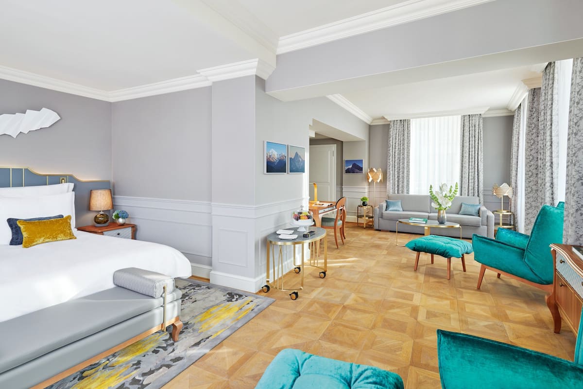 A hotel room with a bed, a sofa, a dining area, and a living area with a view of the mountains.