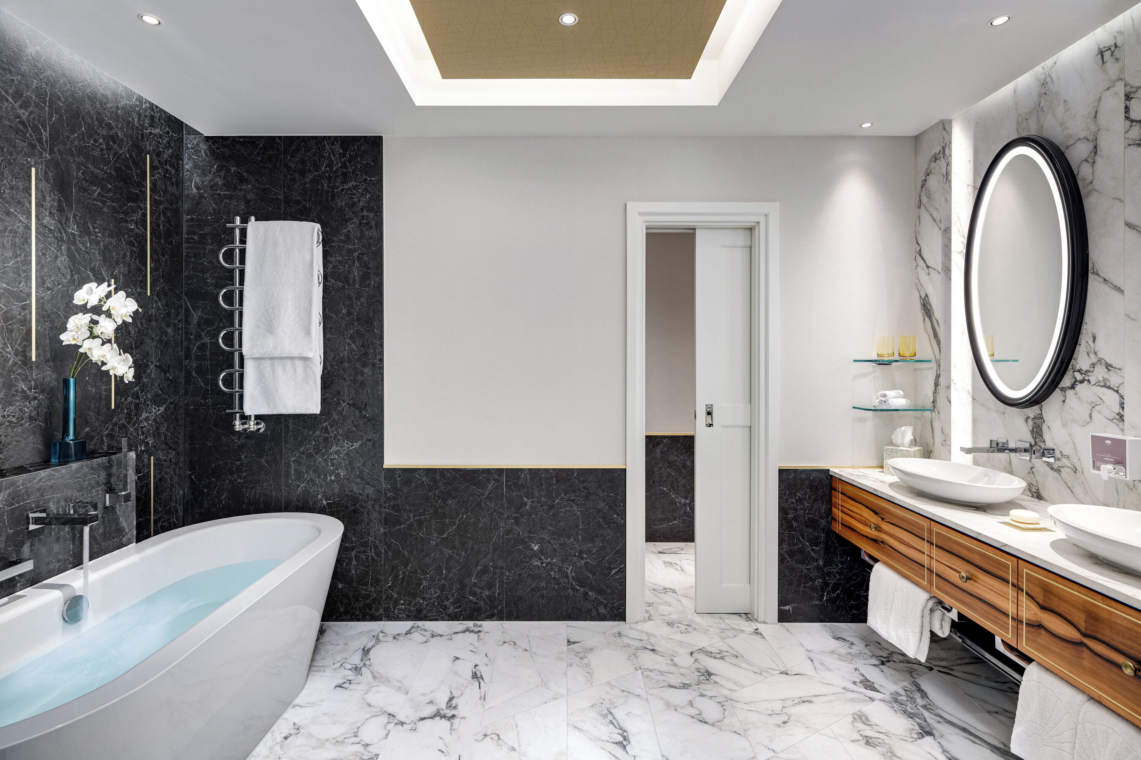 A modern bathroom with a freestanding bathtub, a vanity with a large mirror, and marble flooring.