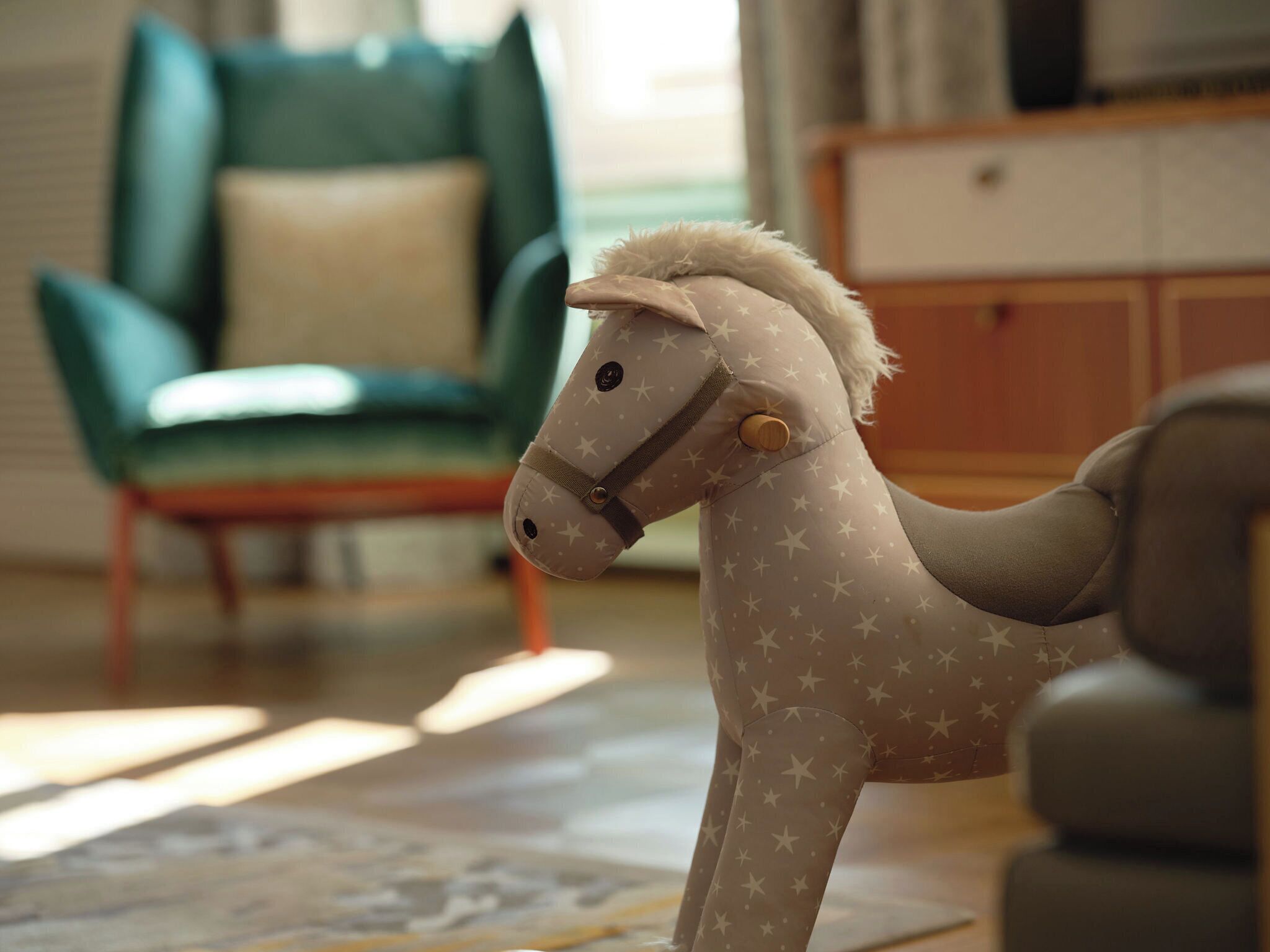 Un cheval en jouet orné d’un motif en étoile, une chaise verte et un meuble en bois dans une pièce.