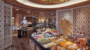 Zona de buffet con diversas opciones de comida y un cocinero preparando alimentos.