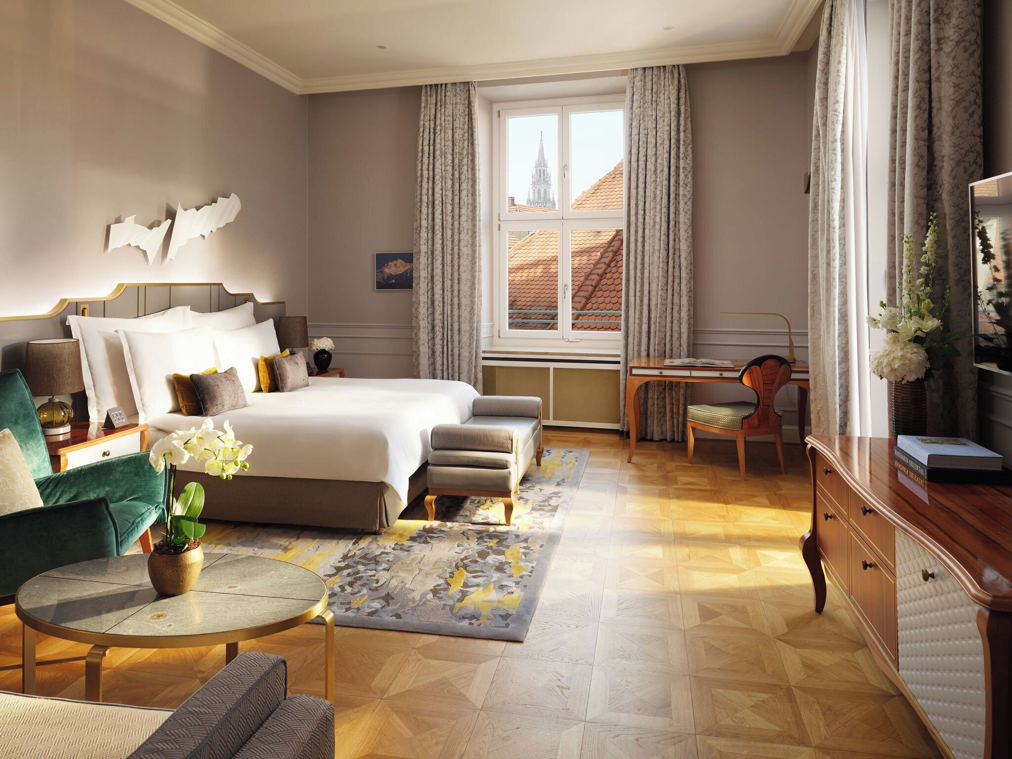 Hotellihuone, jossa on suuri sänky, työpöytä, tuoli, pyöreä pöytä ja ikkunasta avautuva näkymä rakennuksiin.