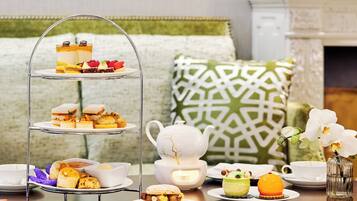 A three-tiered dessert stand with various pastries and a teapot on a table, surrounded by white cups and saucers.
