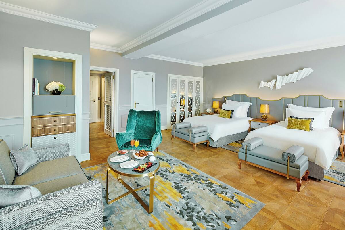 A hotel room with a bed, two bedside tables, a sofa, a chair, and a small table with a tray of food.