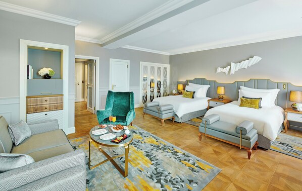 A hotel room with a bed, two bedside tables, a sofa, a chair, and a small table with a tray of food.