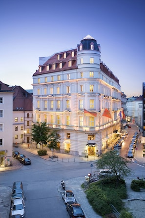 A multi-story hotel with a classic European architectural style, featuring a prominent corner turret and a series of balconies.