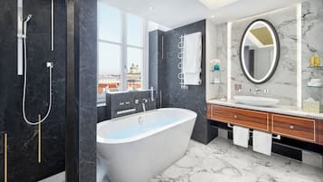 Ett modernt badrum med ett fristående badkar, en stor spegel och utsikt över en stadssiluett genom ett stort fönster.
