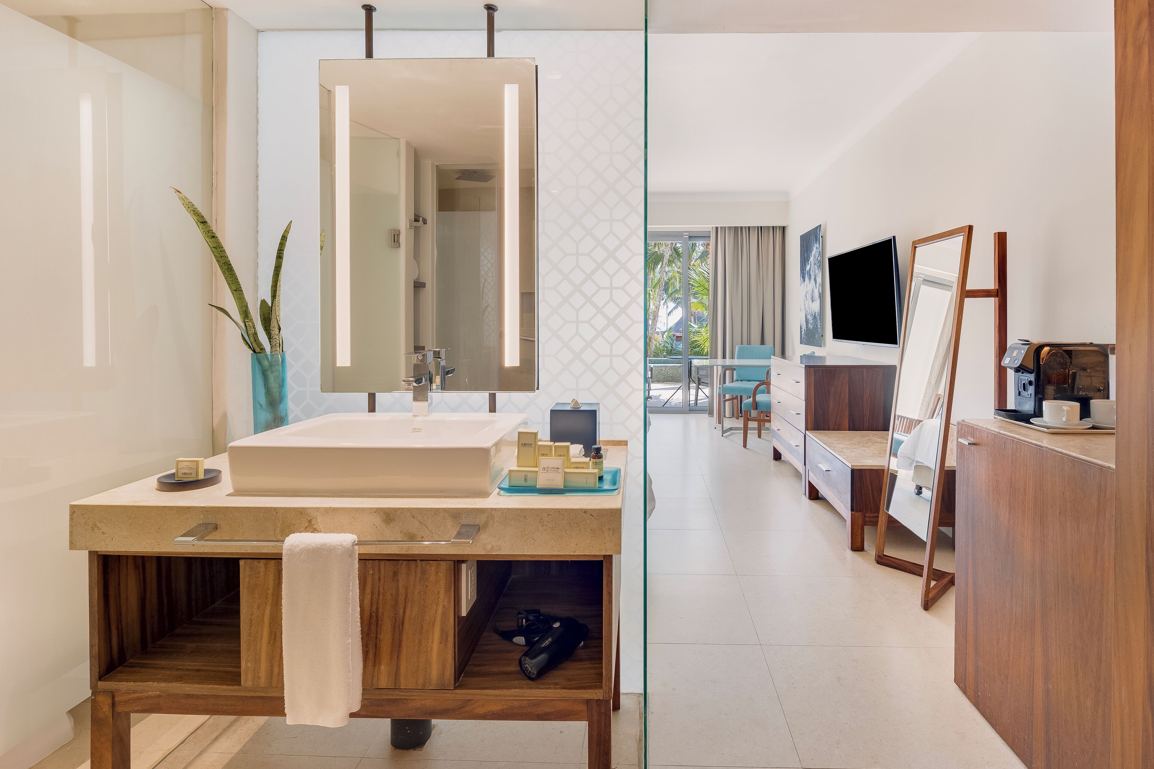 Un baño moderno con un espejo grande, un lavabo y un mueble de tocador. Hay una planta en maceta y una toalla colgada en la pared.
