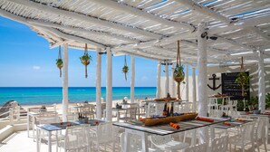 Ein Außenbereich zum Essen mit weißen Stühlen und Tischen, einer Bootsdekoration und Blick auf das Meer.