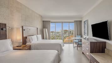 Quarto de hotel com duas camas, uma mesa, uma televisão e varanda com vista para edifícios.