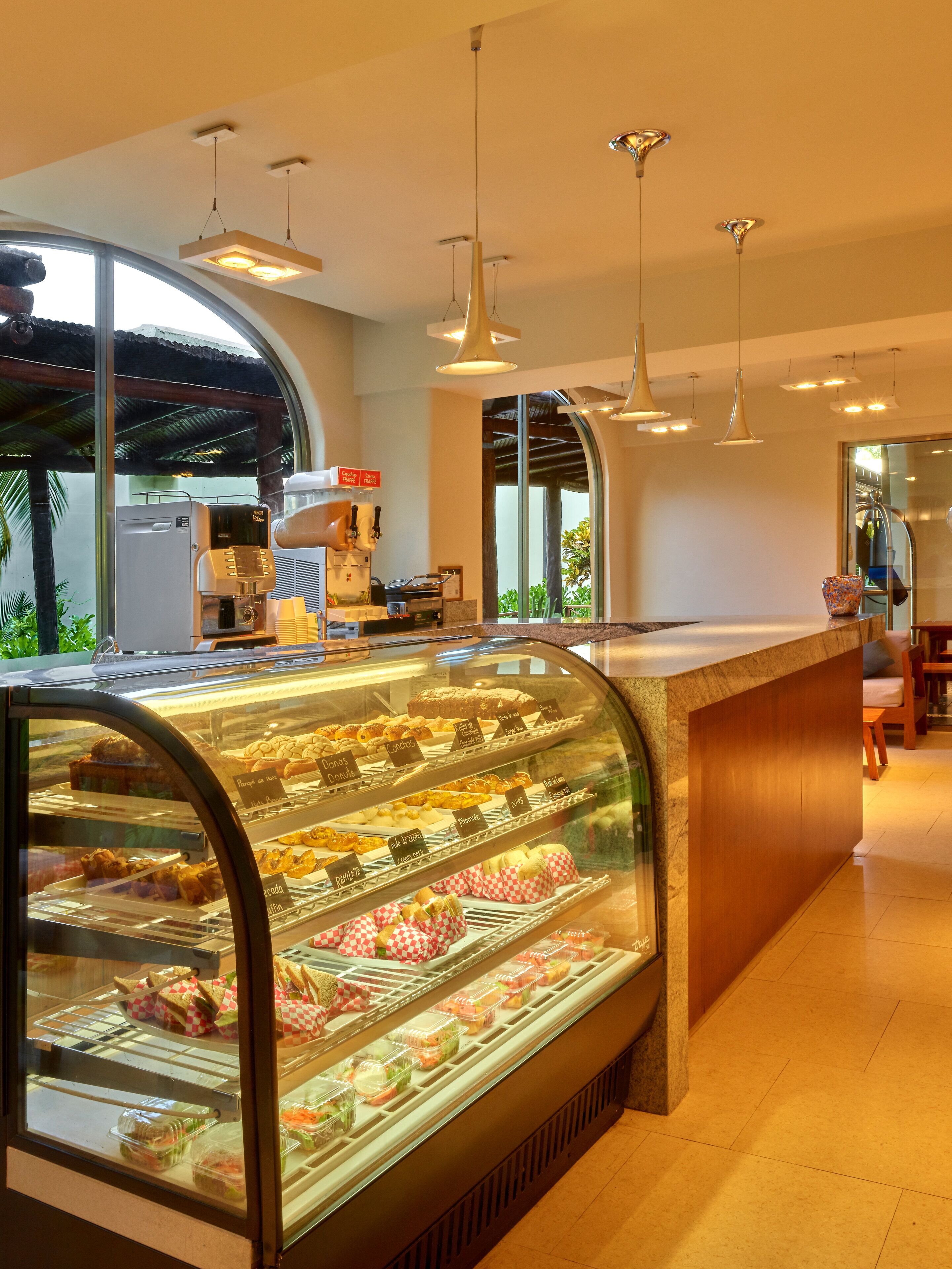 A bakery display case with various baked goods, a coffee machine, and a seating area with a view of the outdoors.