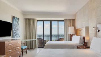 Habitación de hotel con cama, televisor, escritorio, silla y balcón con vista al mar.