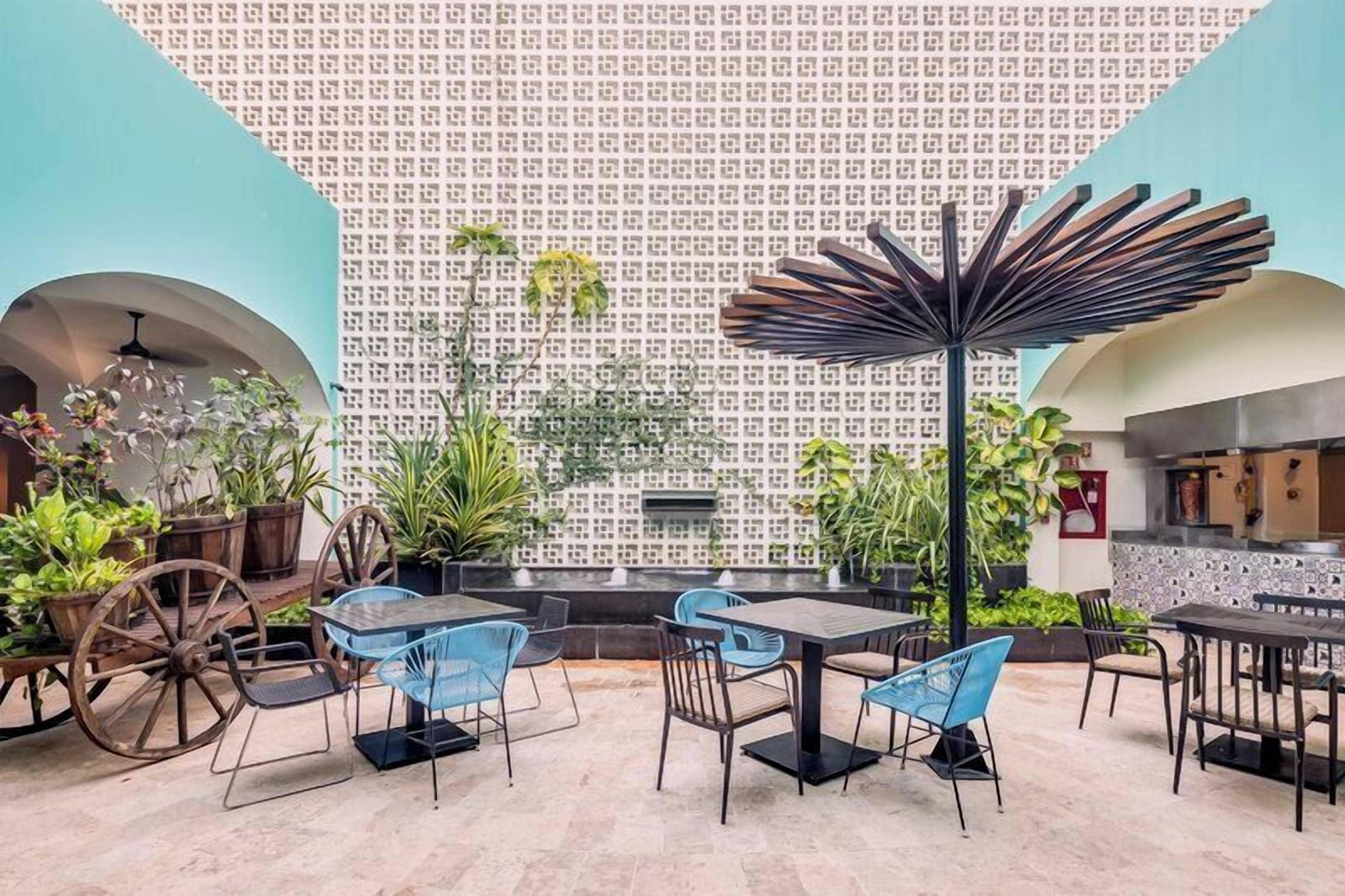 A restaurant with outdoor seating, a patterned wall, and a variety of plants.