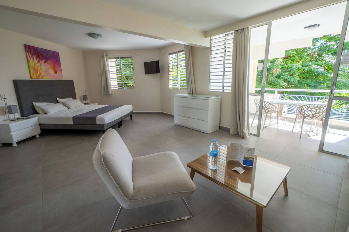 Een moderne hotelkamer met een bed, een stoel, een tafel en een balkon met buitenmeubilair.