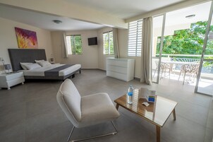 Quarto de hotel com cama, cadeira, mesa, televisão e varanda com mobiliário.
