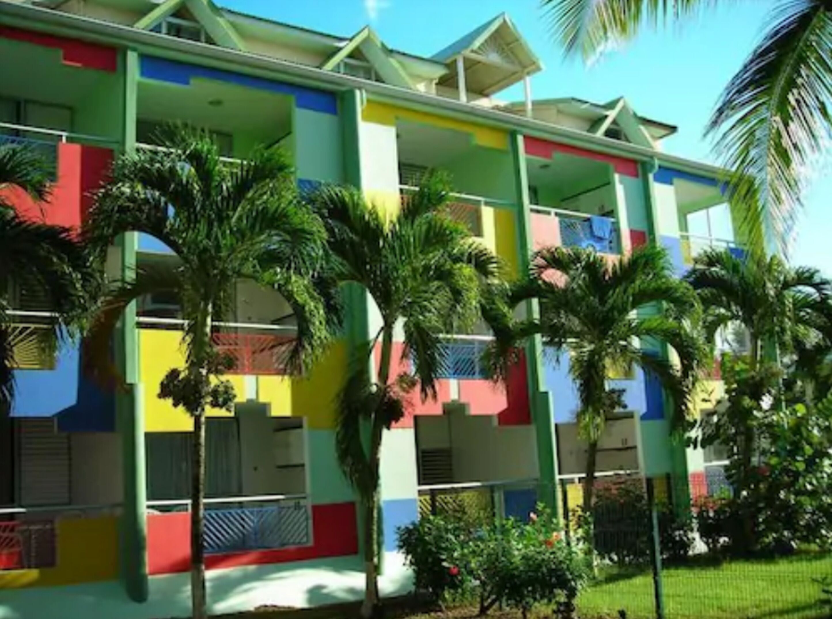 Un bâtiment aux couleurs vives, doté de nombreux balcons et bordé de palmiers.