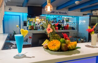 A bar counter with a tropical fruit arrangement, a blue drink, and a decorative light fixture.