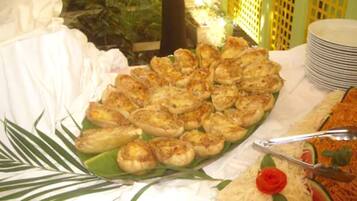 A buffet with various dishes, including a green plate with food, a white tablecloth, and a stack of plates.