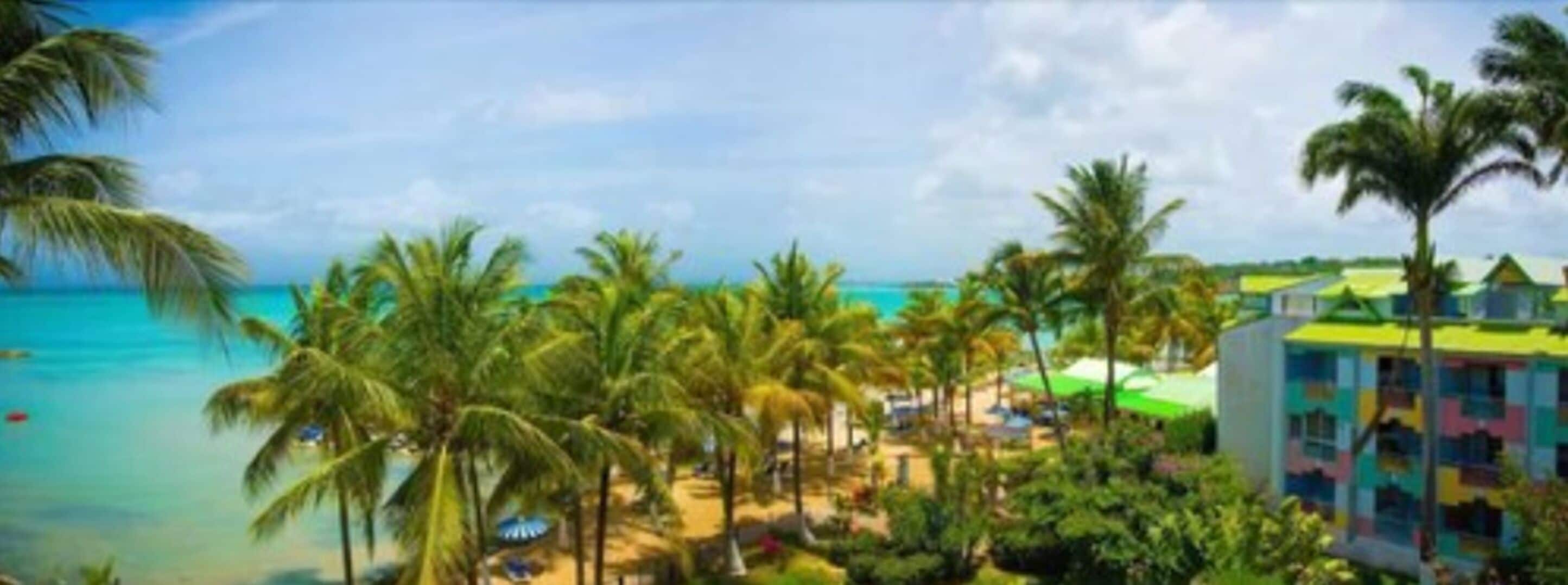 Un complejo turístico en la playa con palmeras, piscina y edificios de colores.
