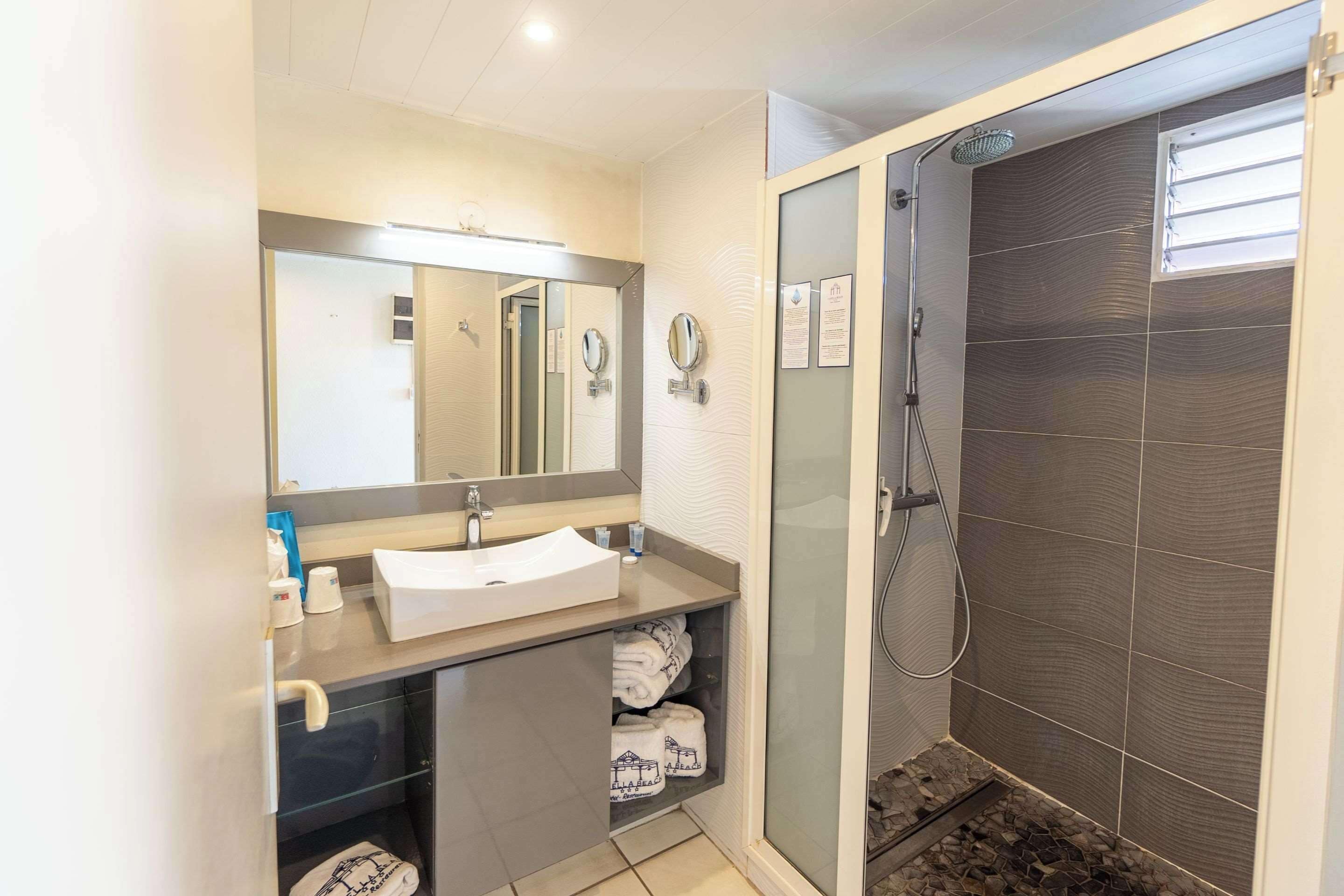 A modern bathroom with a sink, mirror, towel rack, and shower.
