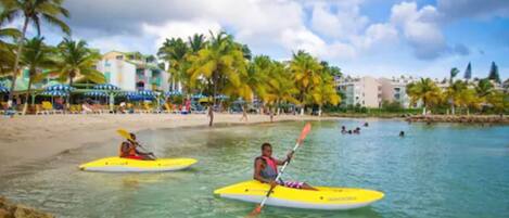 A beach with kayaks, palm trees, and a building in the background.