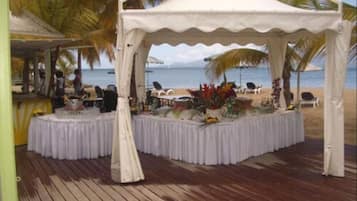 Una carpa frente al mar con una mesa redonda, rodeada de palmeras y sillas de playa.