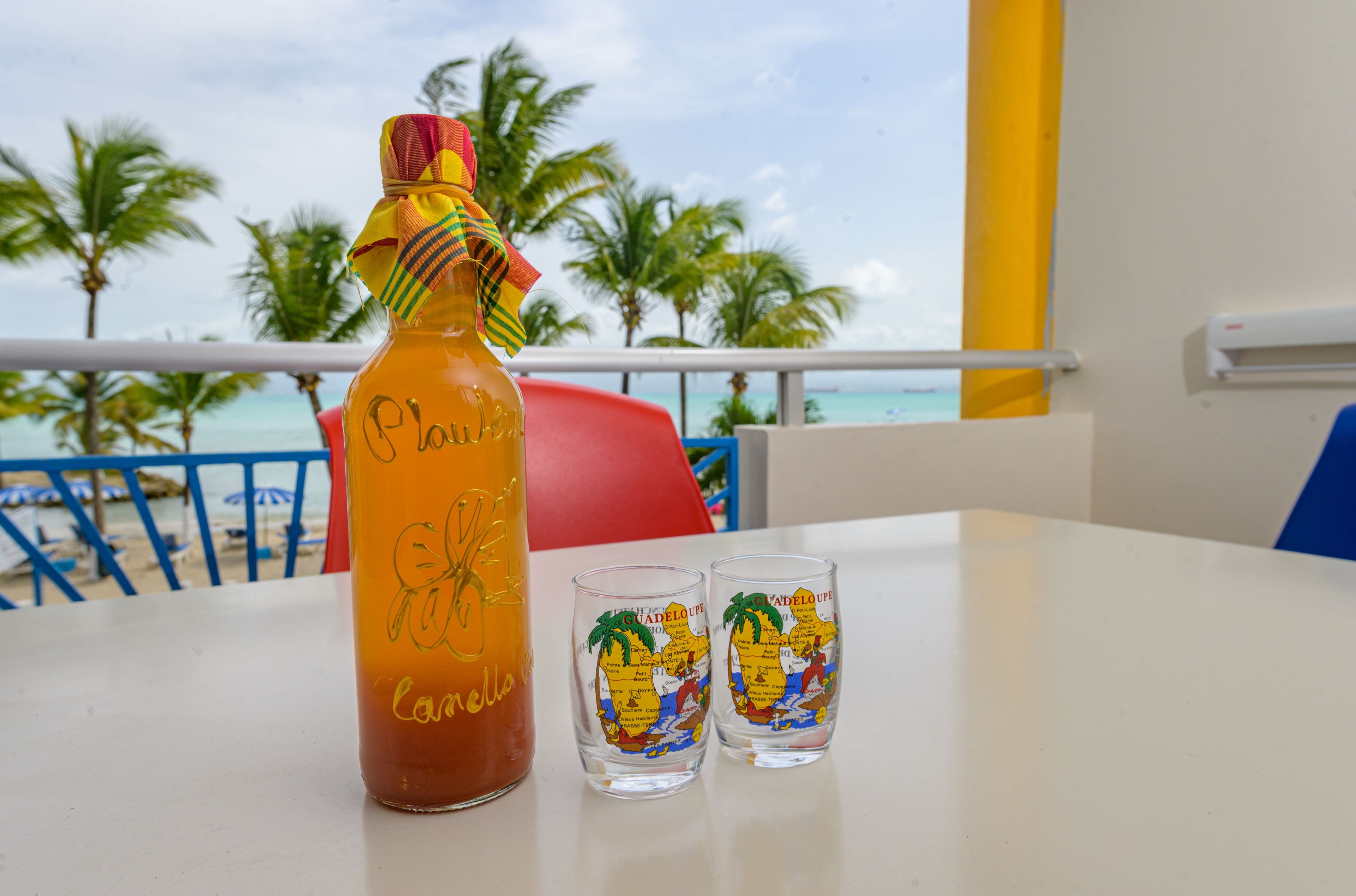 A bottle and two glasses on a table with a view of the beach and palm trees.