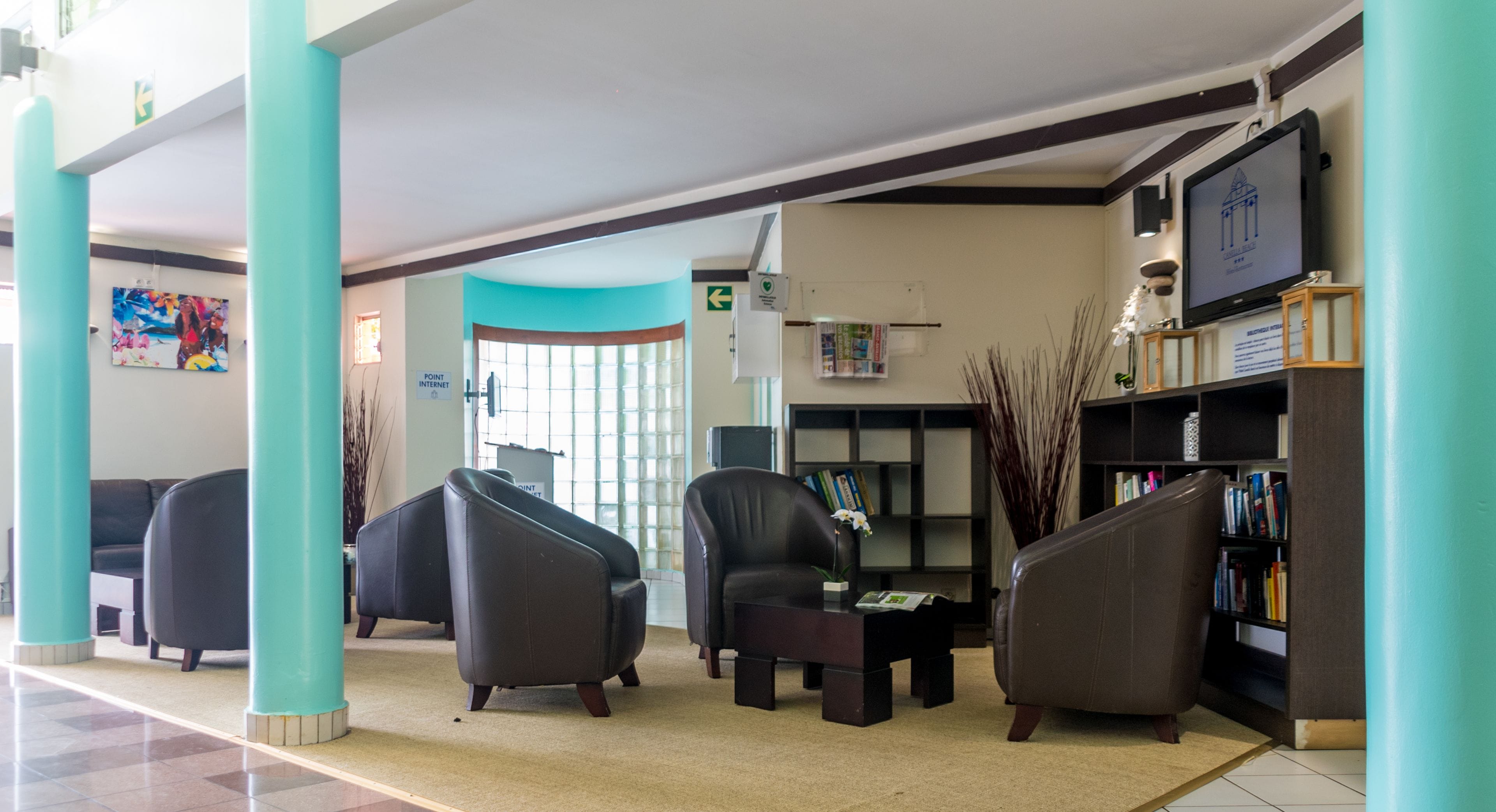 A lobby with teal pillars, leather armchairs, a bookshelf, and a television.