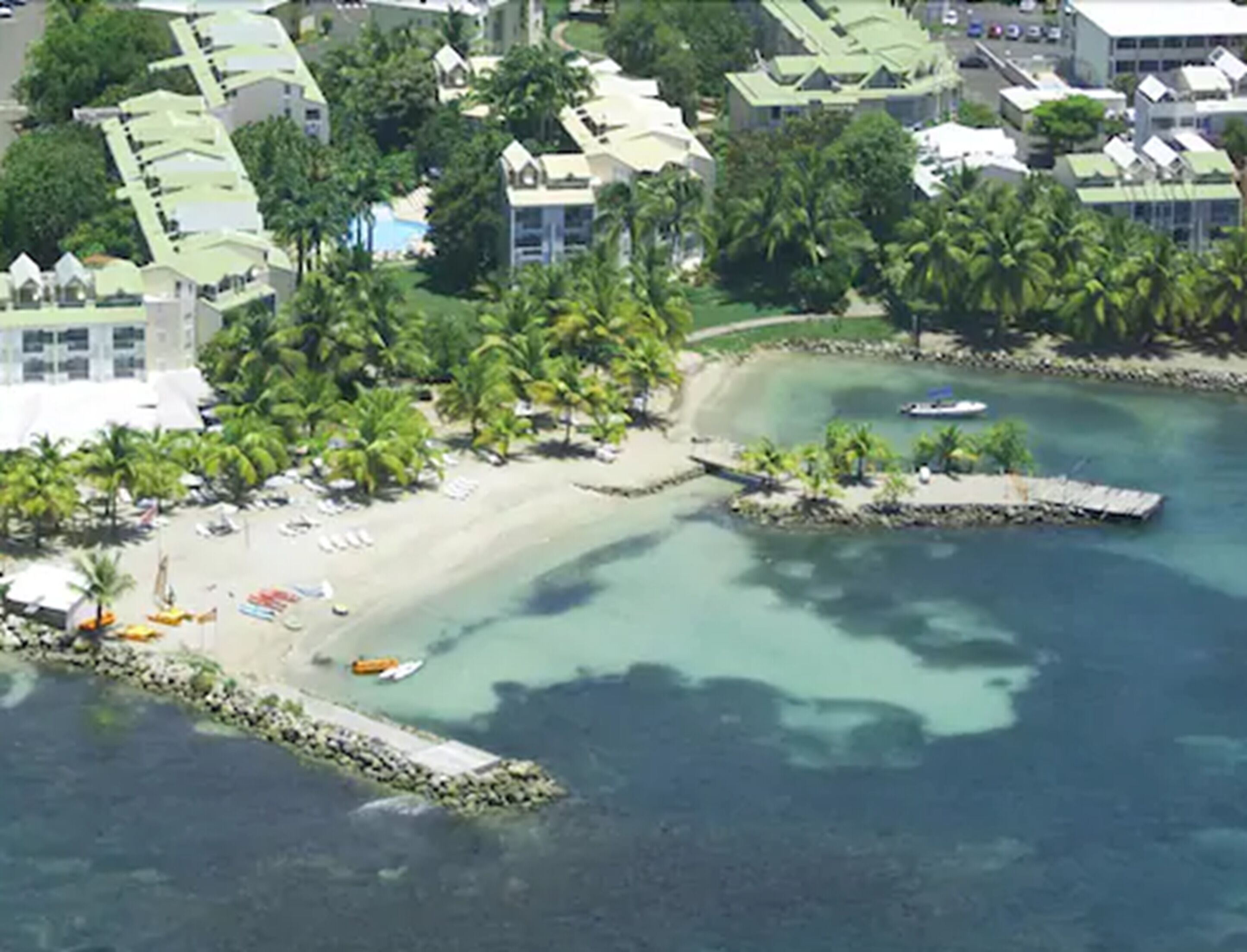 A coastal resort with a sandy beach, palm trees, and a clear blue sea.