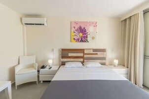 Habitación de hotel con cama, una silla, mesita de noche, aire acondicionado, un cuadro y ventana con cortinas.