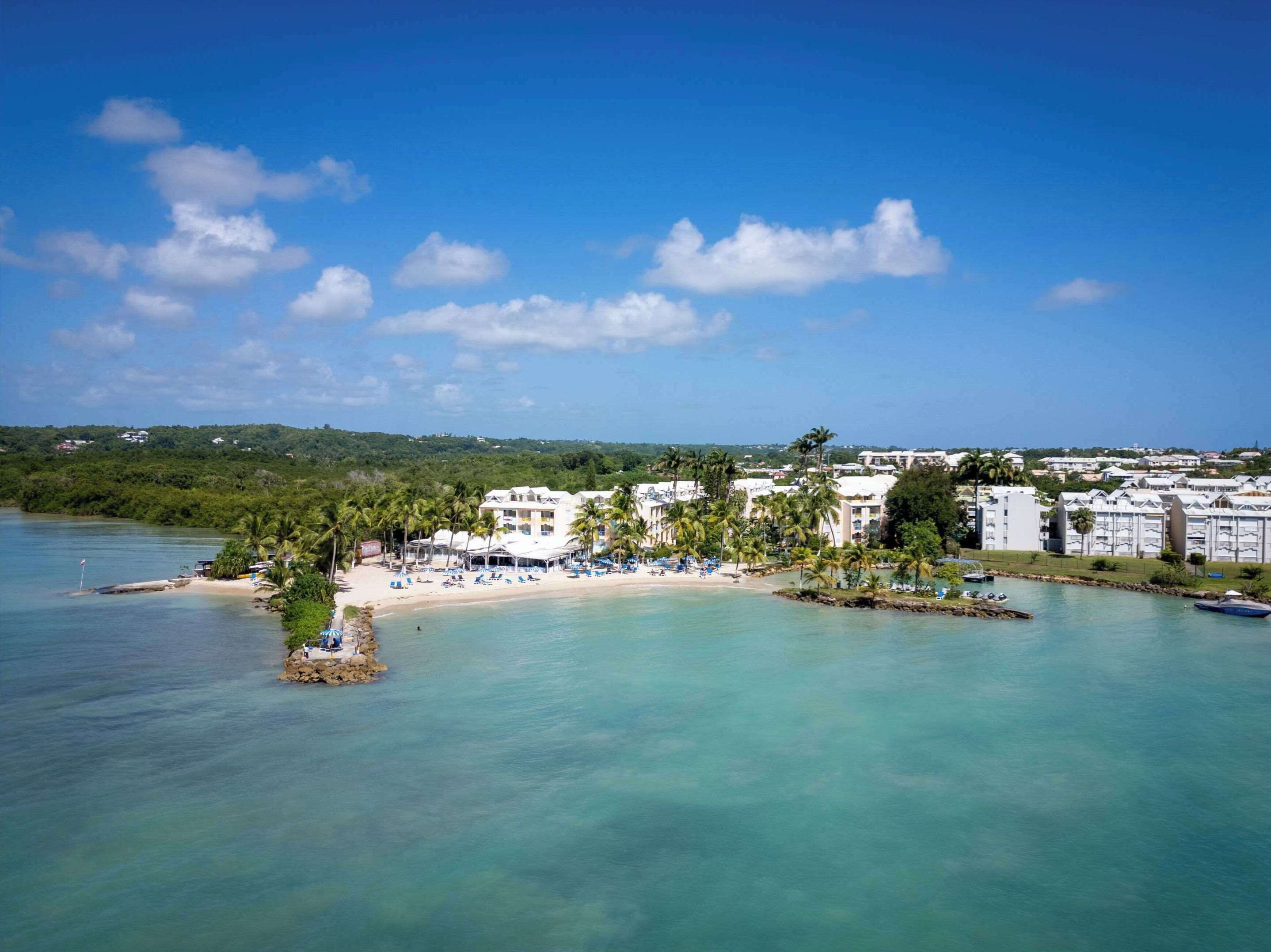 A coastal resort with beachfront villas, clear turquoise waters, and a lush green backdrop.