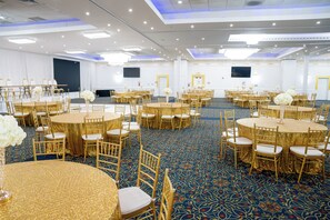 A large banquet hall with round tables and gold chairs, carpeted floor, and a flat-screen TV mounted on the wall. - Metro Points Hotel (Hyattsville)