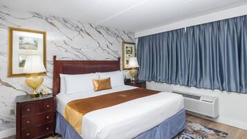 A hotel room with a marble-patterned wall, a bed with a wooden headboard, a blue curtain, and a nightstand with a lamp.