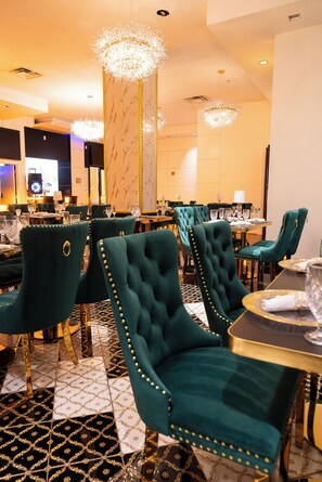 A dining area with green upholstered chairs, marble columns, and chandeliers. - Metro Points Hotel (Hyattsville)