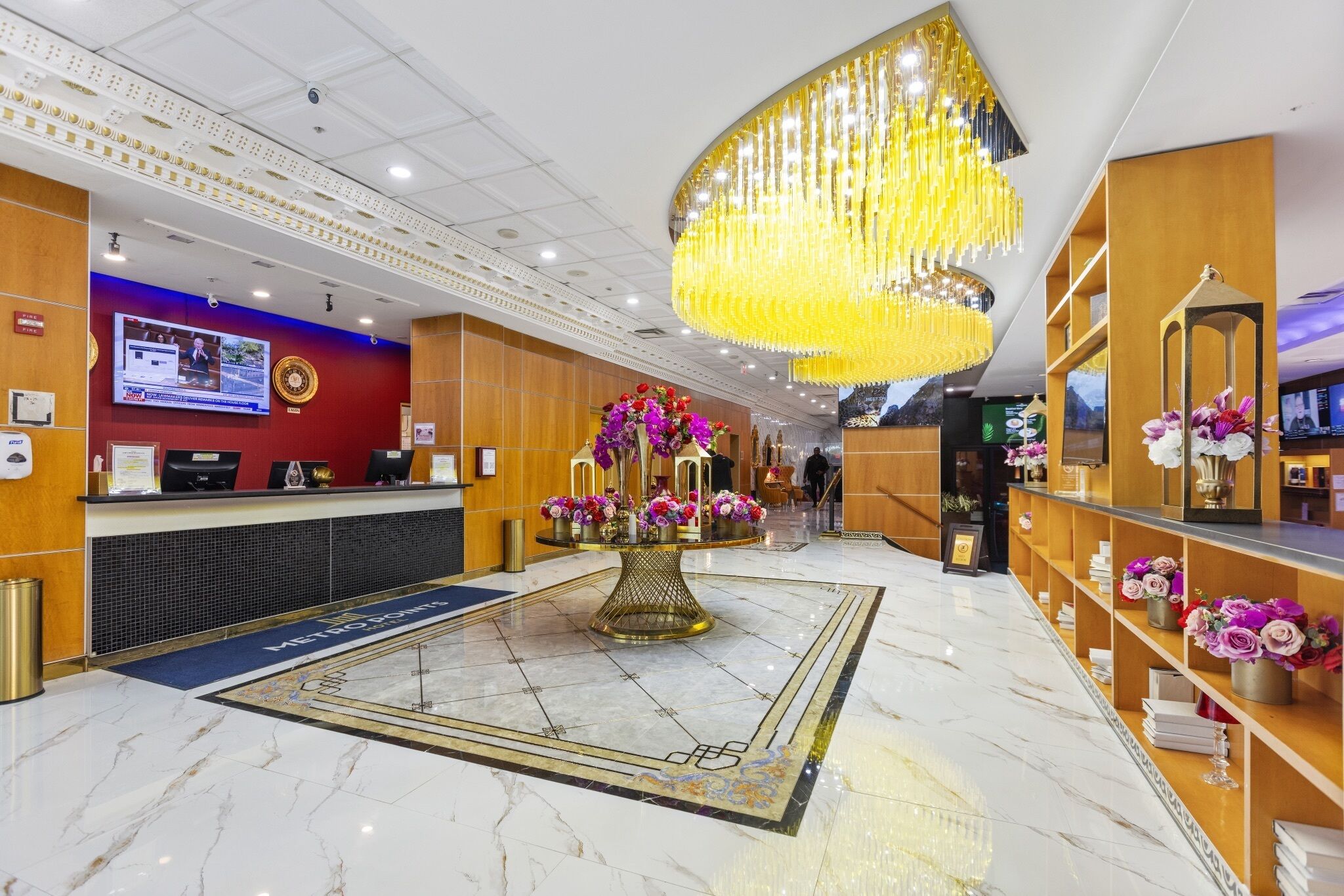 Un vestíbulo de hotel con mostrador de recepción, una lámpara de araña grande y una mesa decorativa con flores.