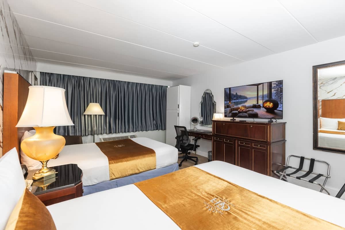Une chambre d’hôtel avec deux lits, un bureau, une chaise, une télévision et une grande fenêtre.