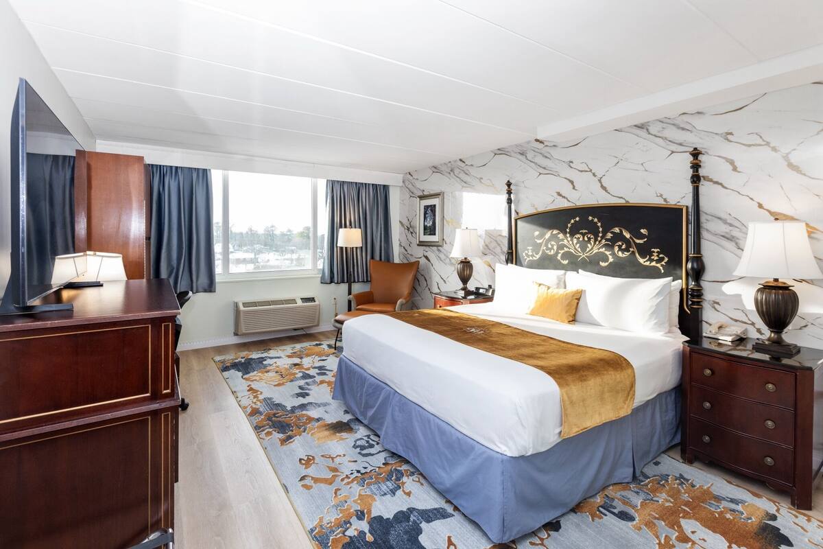 Une chambre d’hôtel avec un grand lit, un bureau, une chaise, une table de chevet et une fenêtre avec des rideaux.